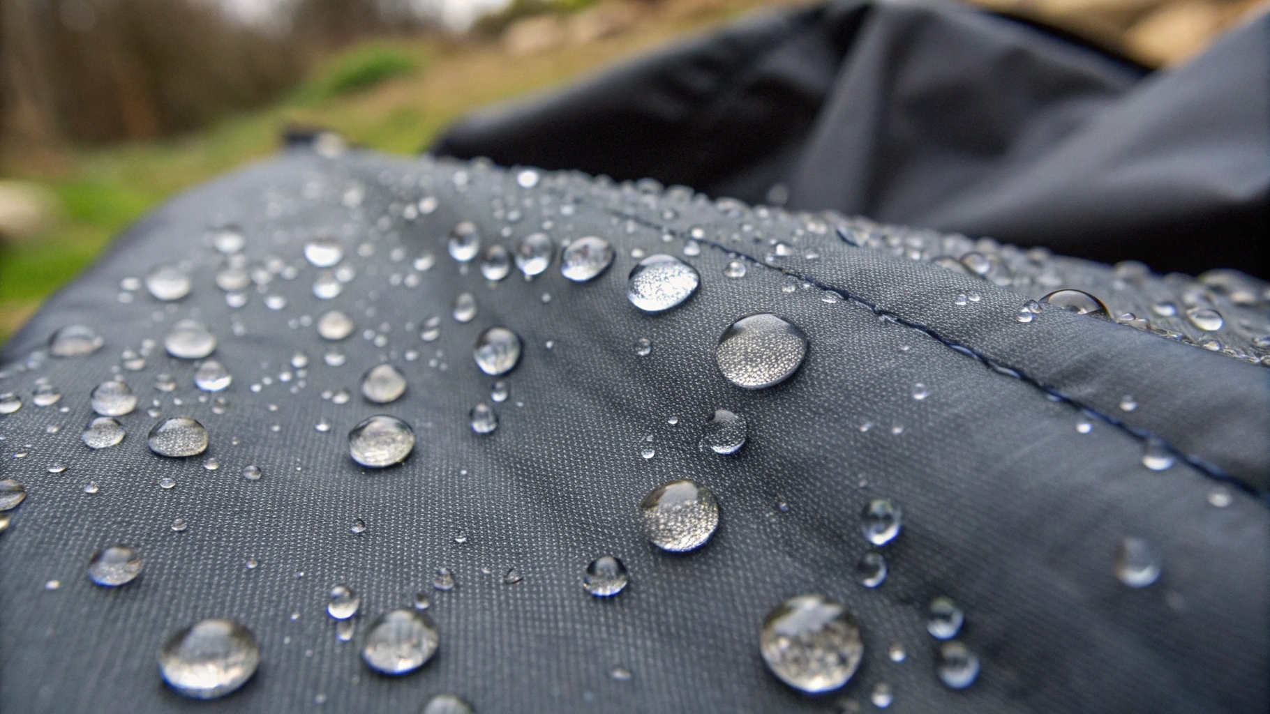 A close-up of water beading on a dark-colored waterproof textile.